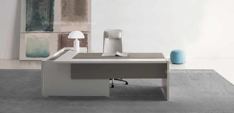 Scrivania direzionale con piano scorrevole lato operatore e modesty panel in melaminico, piano fisso parallelo con spazzolina nera per la gestione dei cavi, mobile di servizio portante con ripiano interno, anta scorrevole soft-closing e serratura, realizzata in conglomerato ligneo spessore 38 mm con finiture cappuccino o nocciola.