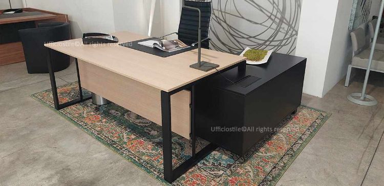 Scrivania da 180 x 100 cm con piano in melaminico appoggiato su struttura metallica con piedini di regolazione, abbinata a mobile di servizio portante sospeso da terra di 10 cm, diviso in due scomparti, con anta scorrevole con serratura, vano portaborse interno, ripiano spostabile e flap integrato sul top con vasca metallica per alloggio prese.