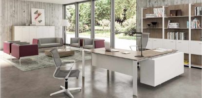 Ambientazione ufficio Linea 607 con scrivania piano Olmo e struttura bianca, allungo con cassettiera portante e vano a giorno, boiserie alta con pannelli in conglomerato ligneo, ripiani in vetro temperato satinato retroverniciato bianco, montanti autoportanti in alluminio estruso verniciato bianco e libreria ufficio a 6 ante sullo sfondo.