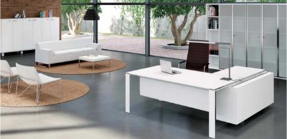 Ambientazione ufficio con scrivania angolare dotata di piano in vetro temperato satinato retroverniciato bianco, box multiuso attrezzato con cassettiera portante, cassetto cancelleria con serratura, vano portaborse e top access con coperchio metallico. Sullo sfondo è presente una libreria alta modulare con 5 ripiani e ante in vetro satinato con telaio in alluminio brillantato.