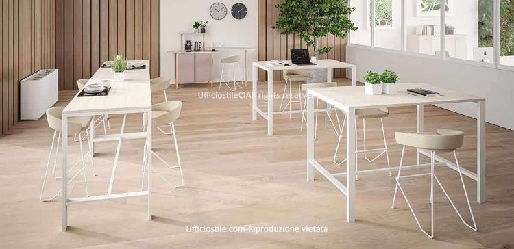 Ambiente ufficio moderno con tavoli alti dotati di struttura in metallo verniciato bianco e top in melaminico chiaro, abbinati a sgabelli imbottiti con schienale basso e base metallica, ideale per break zone, coworking, meeting informali, aree touchdown e spazi di lavoro fluidi e collaborativi.
