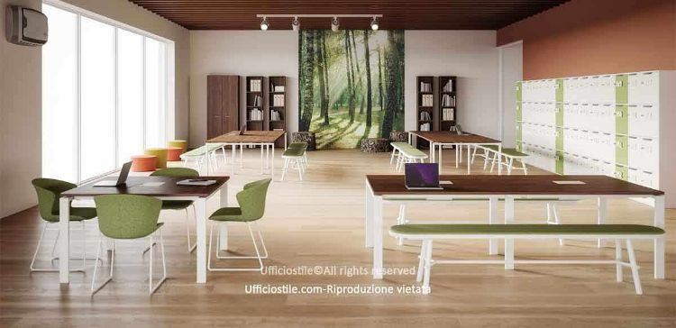 Ambiente collaborativo ispirato alla natura con grandi superfici vetrate, pannello decorativo con immagine forestale, tavoli condivisi, panche, sedute imbottite, postazioni flessibili per lavoro di gruppo o individuale, armadiature e locker modulari per l’organizzazione degli oggetti personali, in tonalità verdi, legno chiaro e accenti naturali.
