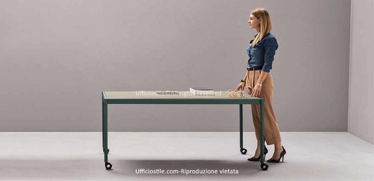 Tavolo plug-&-play su ruote per ufficio, meeting, formazione e catering corporate, con piano ultra-slim in melaminico laccato opaco, telaio perimetrale in alluminio, gambe tool-free, ruote pivotanti frenanti e componenti riciclabili.