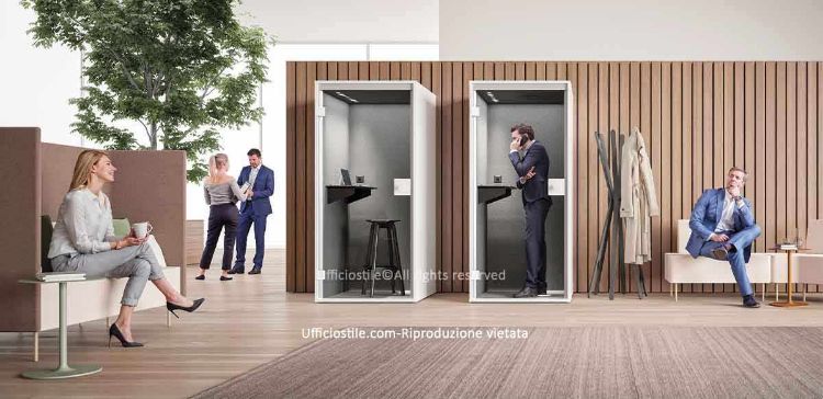 Ambiente ufficio moderno con phone booth acustiche per telefonate e videocall riservate, complete di piano d’appoggio, presa elettrica e illuminazione integrata, affiancate da sedute imbottite ad alto schienale e panche basse con tavolini per aree attesa, relax e coworking, in uno spazio luminoso con finiture in legno chiaro e vegetazione decorativa.