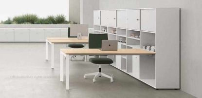 Arredo ufficio operativo composto da una postazione multipla con bench e scrivania da 160 cm agganciati a mobili contenitori alti 115 cm, con scocche in conglomerato ligneo rivestito in melaminico bianco, alluminio o antracite, piedini livellatori, piedini centrali in nylon nero e ante scorrevoli in diverse finiture con bordi ABS in tinta.