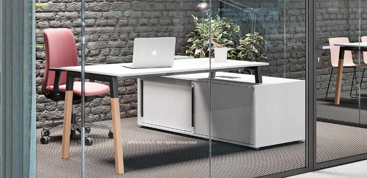Scrivania operativa da 160 x 80 cm in melaminico finitura bianca, disponibile in diverse finiture, appoggiata su mobile di servizio portante con ante scorrevoli, serratura con cilindro estraibile e predisposizione all’elettrificazione, con struttura composta da gambe in metallo e legno massello di frassino naturale verniciato trasparente.