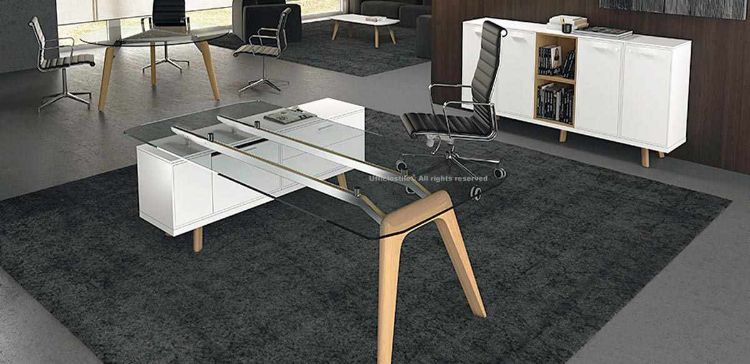 Scrivania a ponte di design con piano in vetro temperato trasparente spessore 12 mm, struttura con due gambe in legno massello, mobile di servizio portante con cassetti con serratura, modulo tecnico e cestello portacavi, completata da credenza contenitore con ante e vani a giorno.