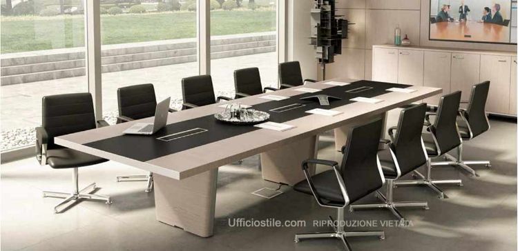 Tavolo riunioni da 421 x 140 cm con piano in legno impiallacciato e inserto in cuoio rigenerato, tre fori con vaschette raccogli cavi, coperchi basculanti in alluminio estruso verniciato o brillantato rivestiti superiormente in cuoio, spazzolini passacavi, gambe con telai in acciaio profilato spazzolato cromo e pannelli esterni in MDF impiallacciato removibili per la discesa dei cavi elettrici.