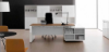 Composizione direzionale con scrivania da 180 cm con piano in conglomerato ligneo spessore 18 mm rivestito melaminico, finiture Noce Maroncelli, Rovere Chiaro, Rovere Scuro o Rovere Naturale, bordi ABS, fianco pannellato e mobile di servizio portante in laminato bianco lucido antigraffio con anta scorrevole, vano portacomputer, griglia di aerazione e top access integrato.
