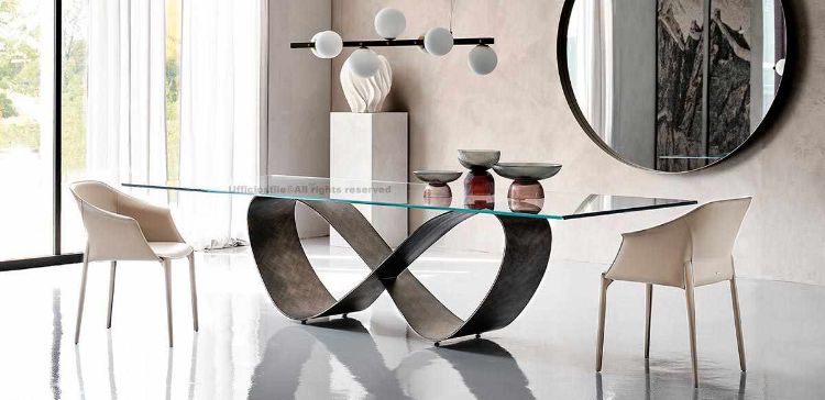 Tavolo sagomato con piano in appoggio in cristallo spessore 15 mm, disponibile in versione trasparente, extrachiaro o extrachiaro con bordi bisellati inversi, base in acciaio titanio, bronzo o finiture Brushed Bronze e Brushed Grey per sale riunioni e ambienti direzionali.