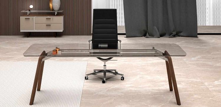 Scrivania direzionale di design con piano in vetro temperato trasparente spessore 12 mm, struttura in legno finitura rovere tabacco, gambe in massello stondate e verniciate a poro aperto, abbinata a mobile contenitore con anta, due cassetti e top in vetro coordinato.